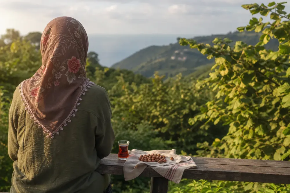 Person seen from behind on a bench in a Giresun hazelnut orchard, with a handful of hazelnuts and tea