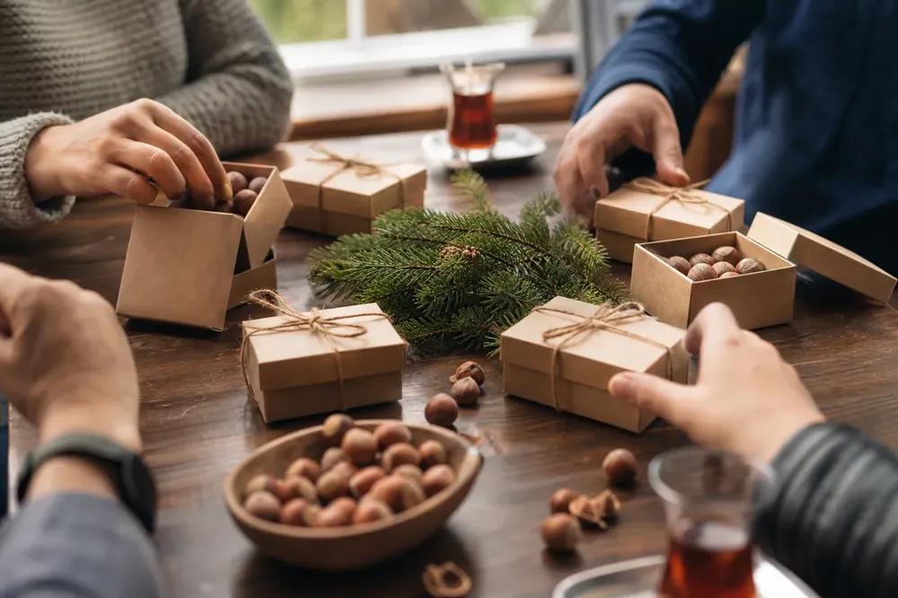Hands reaching for roasted hazelnuts in open gift boxes on a meeting table with tea glasses